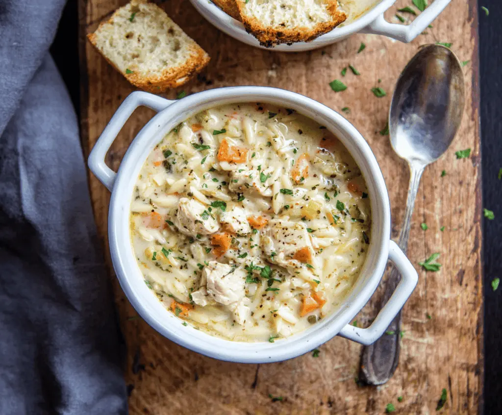 A bowl of creamy chicken orzo soup garnished with fresh herbs, featuring tender chicken, orzo pasta, and a rich, flavorful broth.
