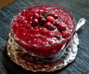 A jar of homemade Cranberry Jezebel Sauce with fresh cranberries and citrus slices.