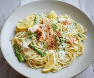 Delicious salmon pasta with a rich lemon cream sauce and fresh herbs on a white plate.