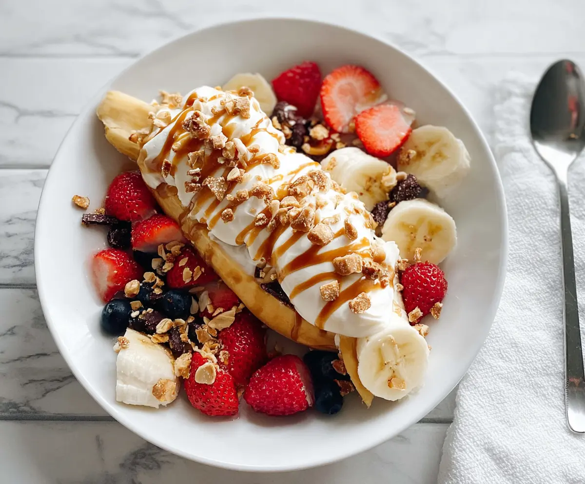 Colorful breakfast banana split with fresh bananas, strawberries, blueberries, and yogurt served in a glass bowl.