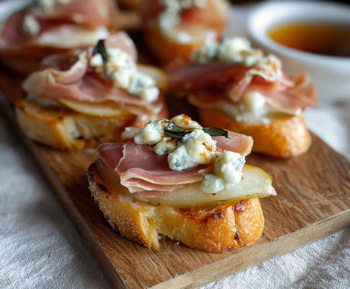 Delicious Prosciutto Pear Gorgonzola Crostini featuring crispy crostini topped with prosciutto, pear slices, and creamy Gorgonzola cheese.