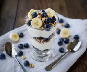 Layered blueberry, banana, and yogurt parfait in a clear glass, garnished with fresh blueberries.