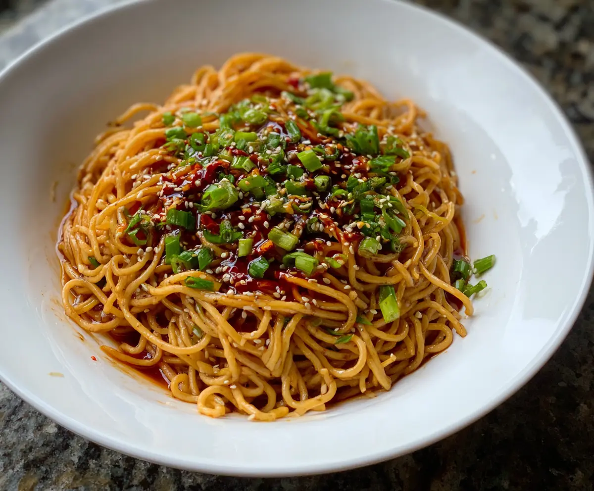 Delicious Cold Spicy Szechuan Sesame Noodles garnished with sesame seeds and green onions on a white plate.