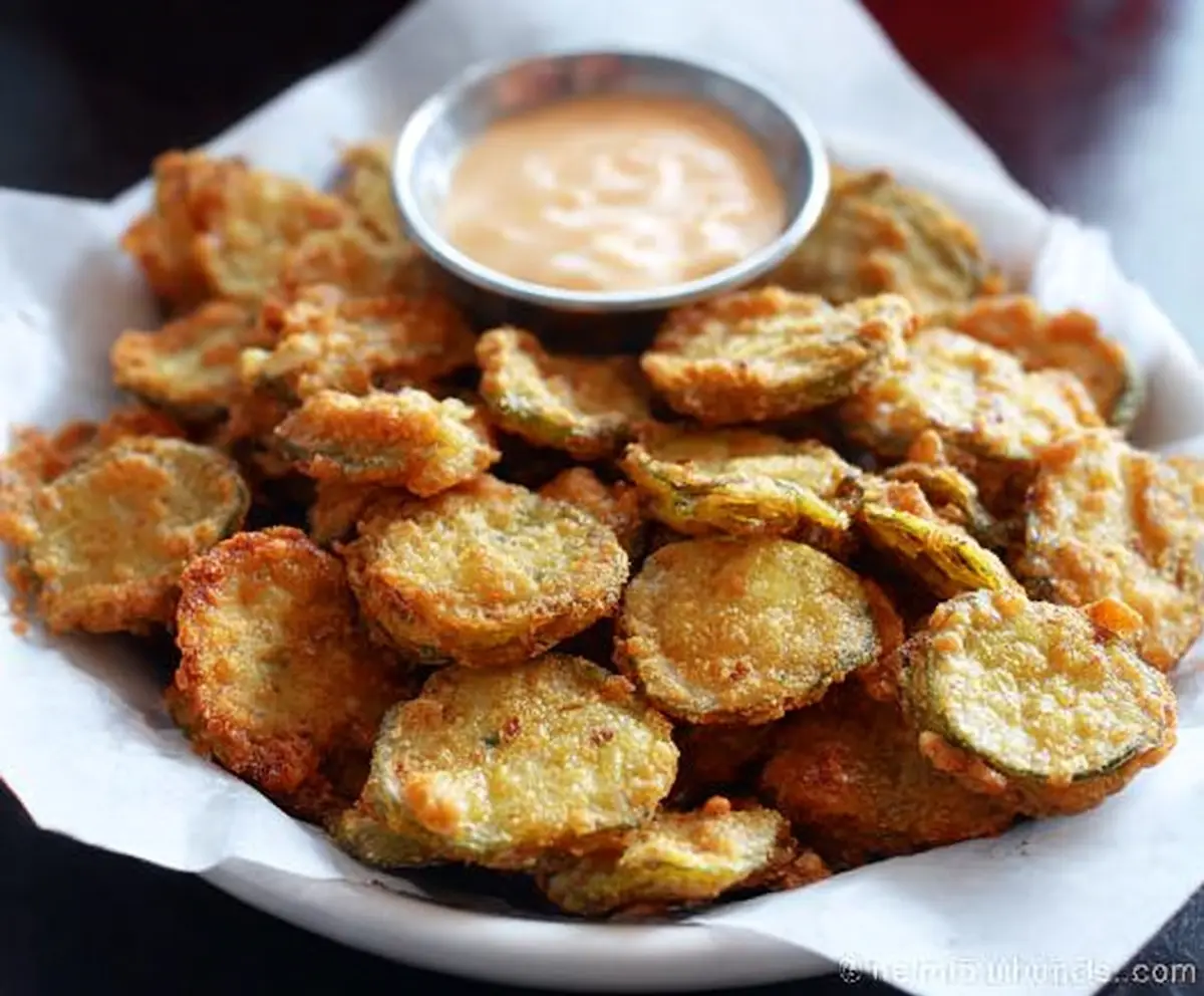 Crispy fried pickles served with dipping sauce on a rustic plate
