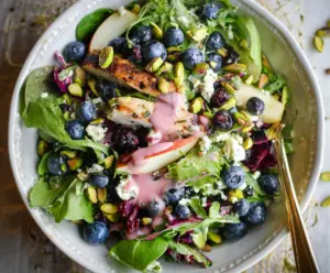 Fresh Blueberry and Pistachio Spring Salad served in a bowl with vibrant greens and edible flowers