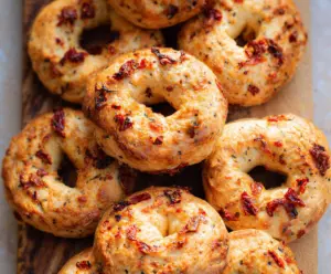 Delicious Sun-Dried Tomato Sourdough Bagels on a wooden board, showcasing a golden-brown crust and vibrant tomato bits inside.