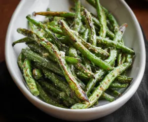 Delicious roasted green beans garnished with herbs on a white plate, perfect for a healthy side dish.