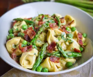 Delicious tortellini pasta with peas, asparagus, and crispy bacon garnished with herbs.
