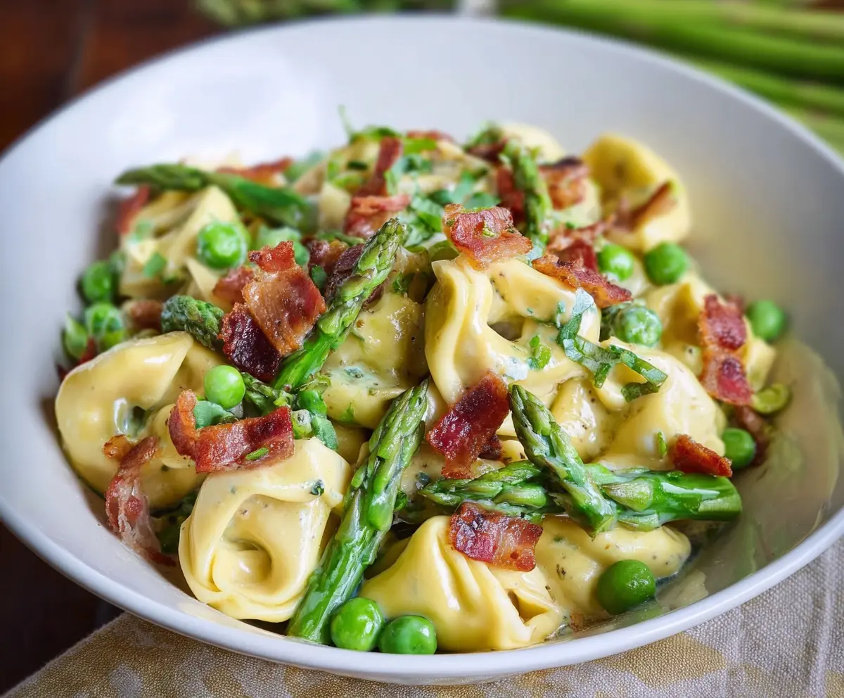 Delicious tortellini pasta with peas, asparagus, and crispy bacon garnished with herbs.